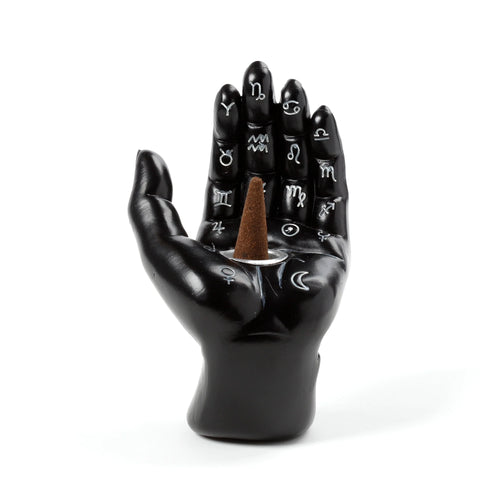 Front view of a black decorative hand incense burner, featuring white astrological symbols on the fingers and palm, holding a brown incense cone in a silver holder.