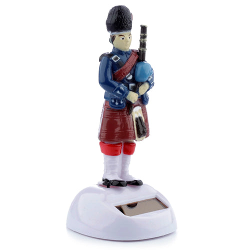 Front view of a Novelty Scottish Piper Solar Powered Pal figurine. The piper wears a blue jacket and red kilt, holding bagpipes, standing on a white base with a visible solar panel.