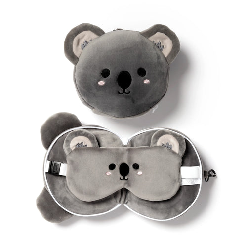 Overhead view of a grey plush koala travel pillow and matching eye mask set. The travel pillow is shown both as a compact round koala head with embroidered facial features and unzipped, revealing the neck pillow and eye mask with an adjustable strap.