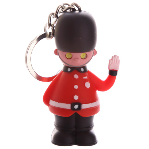 Front view of a British Guardsman novelty keyring, featuring a stylised figure in a red uniform with white buttons and belt details, a black bearskin hat, and yellow circular eyes, with one hand raised, attached to a silver-coloured metal chain and keyring.