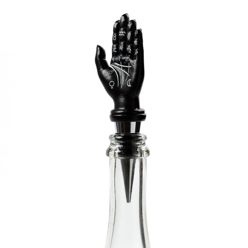 Front view of a black hand novelty bottle stopper with white astrological and palmistry symbols, inserted into a clear glass bottle.