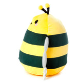 Angled view of a plush toy bee with a yellow and dark green striped body. It features small black embroidered eyes, pink blush details on its cheeks, black antennae with yellow fluffy tips, and shimmery silver wings. A white product tag is visible near the base.