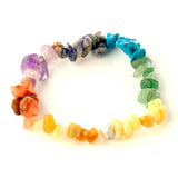 Front view of a chakra gemstone bracelet featuring polished, irregularly shaped stones in a colorful spectrum including purple, blue, green, yellow, orange, and red hues, displayed on a white background.