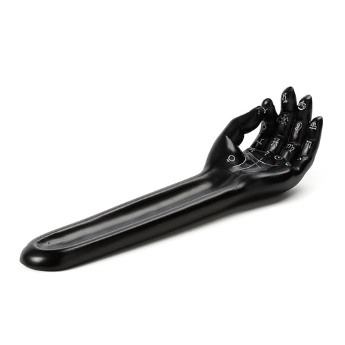 Angled view of a black decorative incense ashcatcher shaped like a mantric hand or tarot palm, featuring white symbolic markings on its surface.