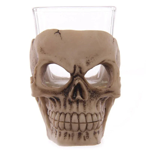 Front view of a gruesome skull shot glass, featuring a bone-coloured casing with cracked detailing and a clear glass insert.