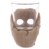 Gruesome Skull Mini Shot Glass, front view, showing a clear glass insert within a light beige, cracked skull-shaped holder with prominent eye sockets.