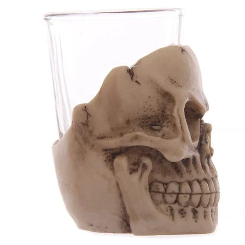 Angled view of a gruesome skull mini shot glass, featuring a detailed, bone-coloured skull with visible eye socket, nose cavity, and teeth, partially encasing a clear glass.
